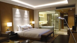 A modern hotel room with a large bed, bedside lamps, a glass shower enclosure, and a bedside table with a lamp.