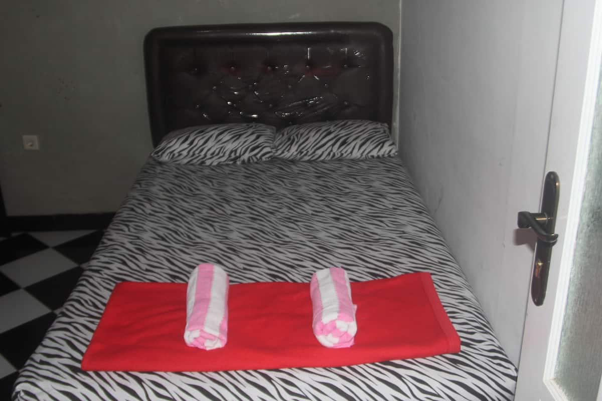 A single bed with a zebra print bedspread and two rolled towels on a red mat.