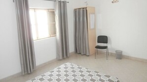 A room with a bed, a chair, a small cabinet, and a window with curtains. - SolaCyber (Boa Vista)