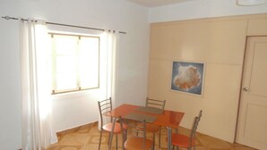 A dining area with a table and chairs, a window with curtains, a door, and a wall-mounted picture. - SolaCyber (Boa Vista)