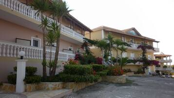 A row of two-story buildings with balconies, surrounded by landscaped gardens with palm trees and flowering plants.
