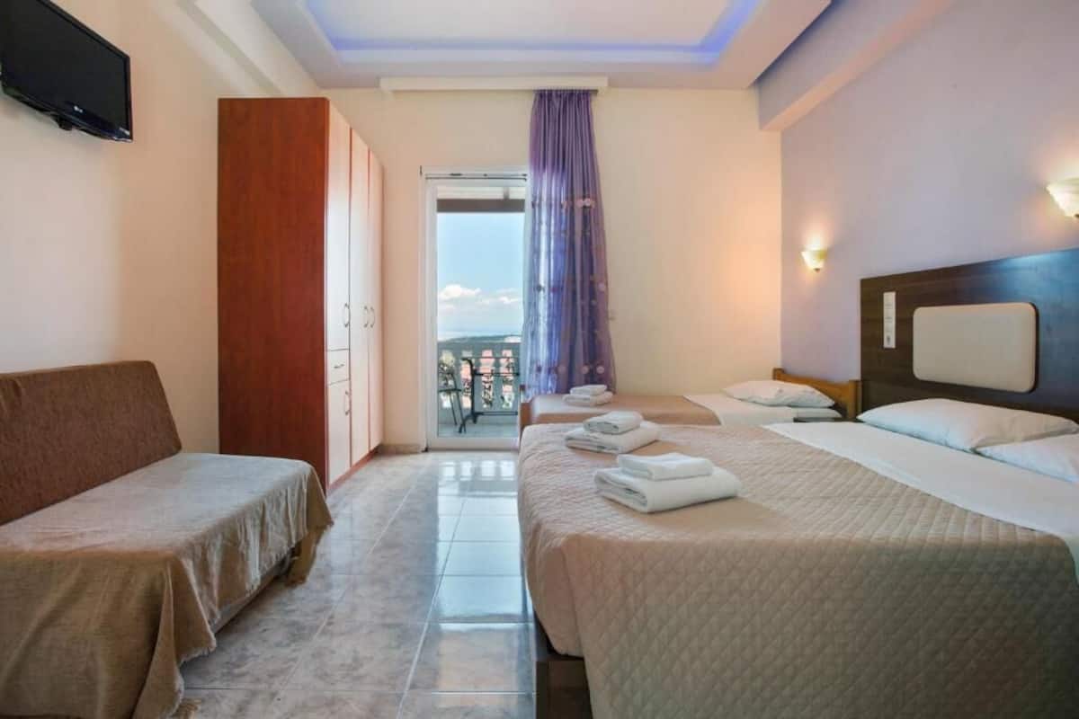 A hotel room with two single beds, a sofa, a TV, and a balcony with a view.
