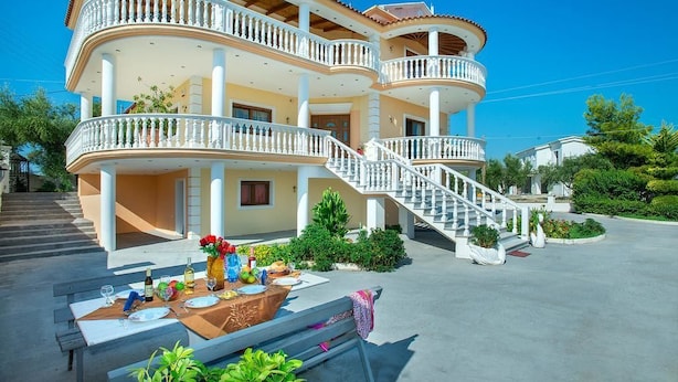 A multi-story building with balconies, a staircase, and a dining area set up outside. - Zante View Studios (Zakynthos)