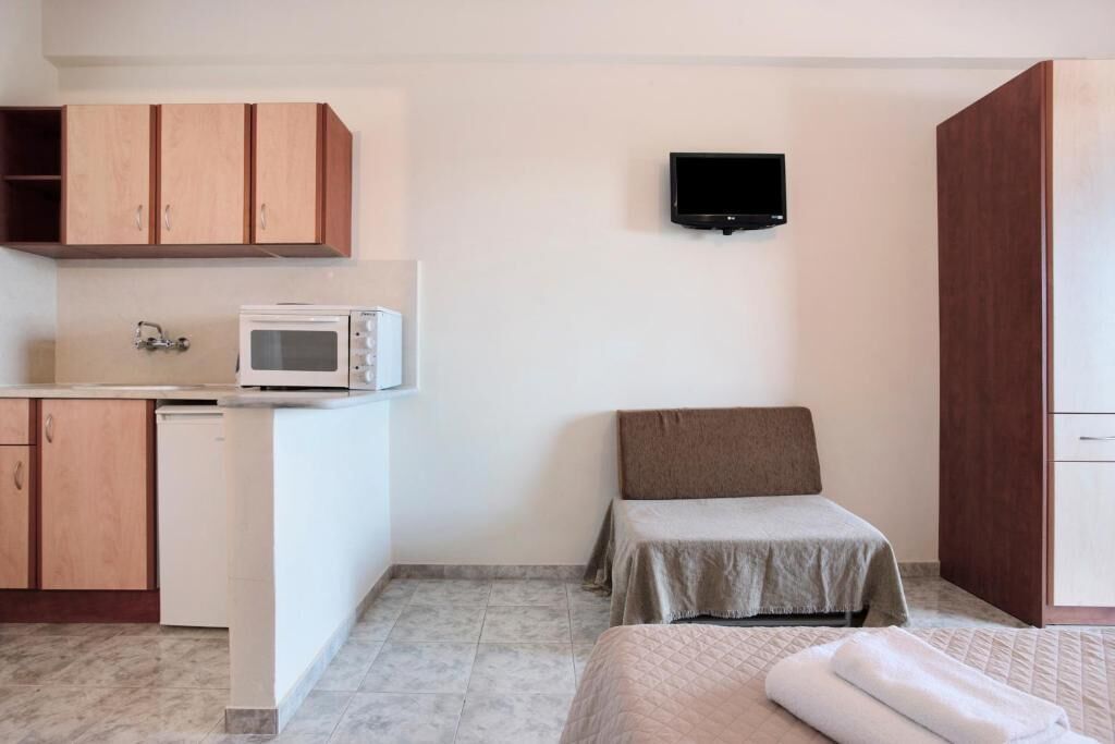 A compact room with a kitchenette, a bed, and a TV mounted on the wall.