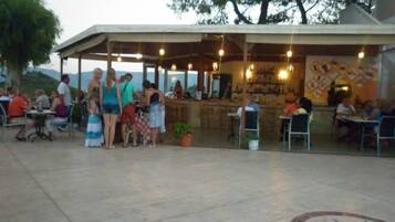 An outdoor dining area with tables and chairs, a covered seating area, and a bar.