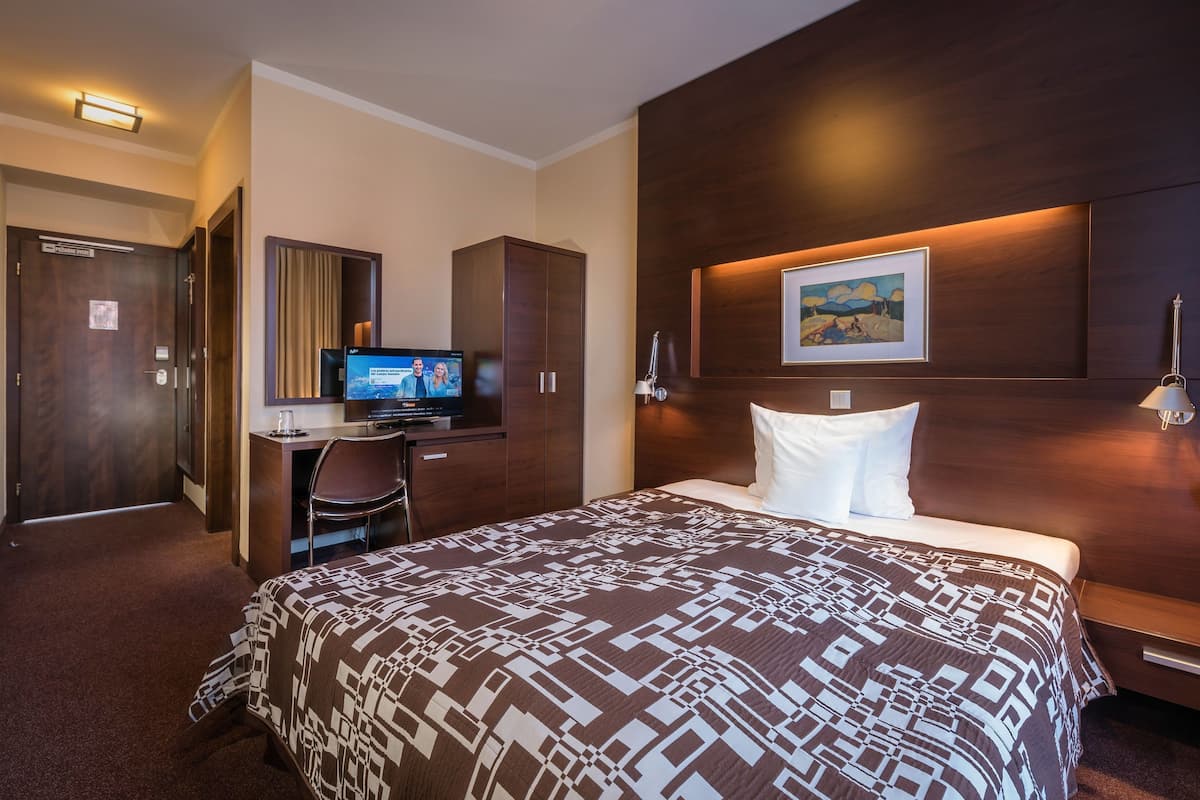 A hotel room with a large bed, a desk with a computer, a TV, and a framed picture on the wall.