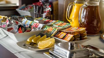 A breakfast buffet with various food items, including packaged snacks, fresh fruit, and a pitcher of orange juice.