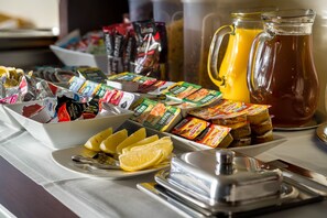 Un bufé de desayuno con diversos alimentos, incluyendo aperitivos empacados, fruta fresca y una jarra de jugo de naranja.