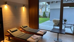 Un spa moderno con dos sillones reclinables, una mesita y vistas a un jardín a través de un ventanal.
