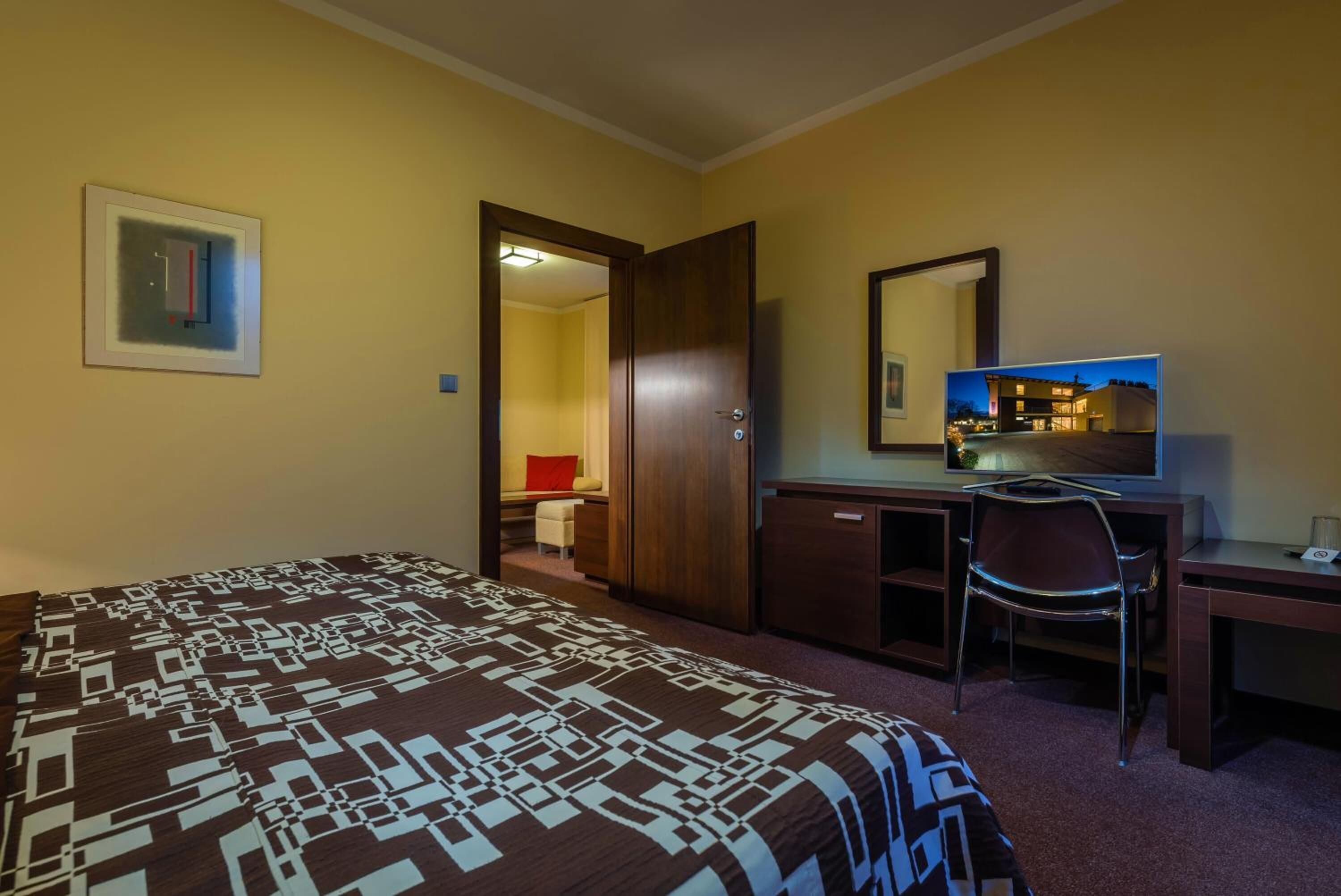 A hotel room with a bed, a desk, a chair, a wardrobe, and a mirror.