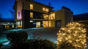 Un hotel de diseño moderno, con una estructura de dos pisos, un espacio exterior cubierto y un árbol de Navidad con luces.