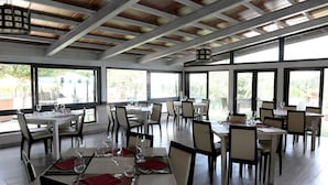 Un restaurante con varias mesas y sillas, ventanas amplias y un techo alto con vigas a la vista.