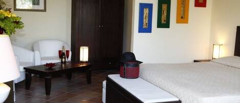 Quarto de hotel com cama, escrivaninha, cadeira, armário e parede com obras de arte emolduradas.