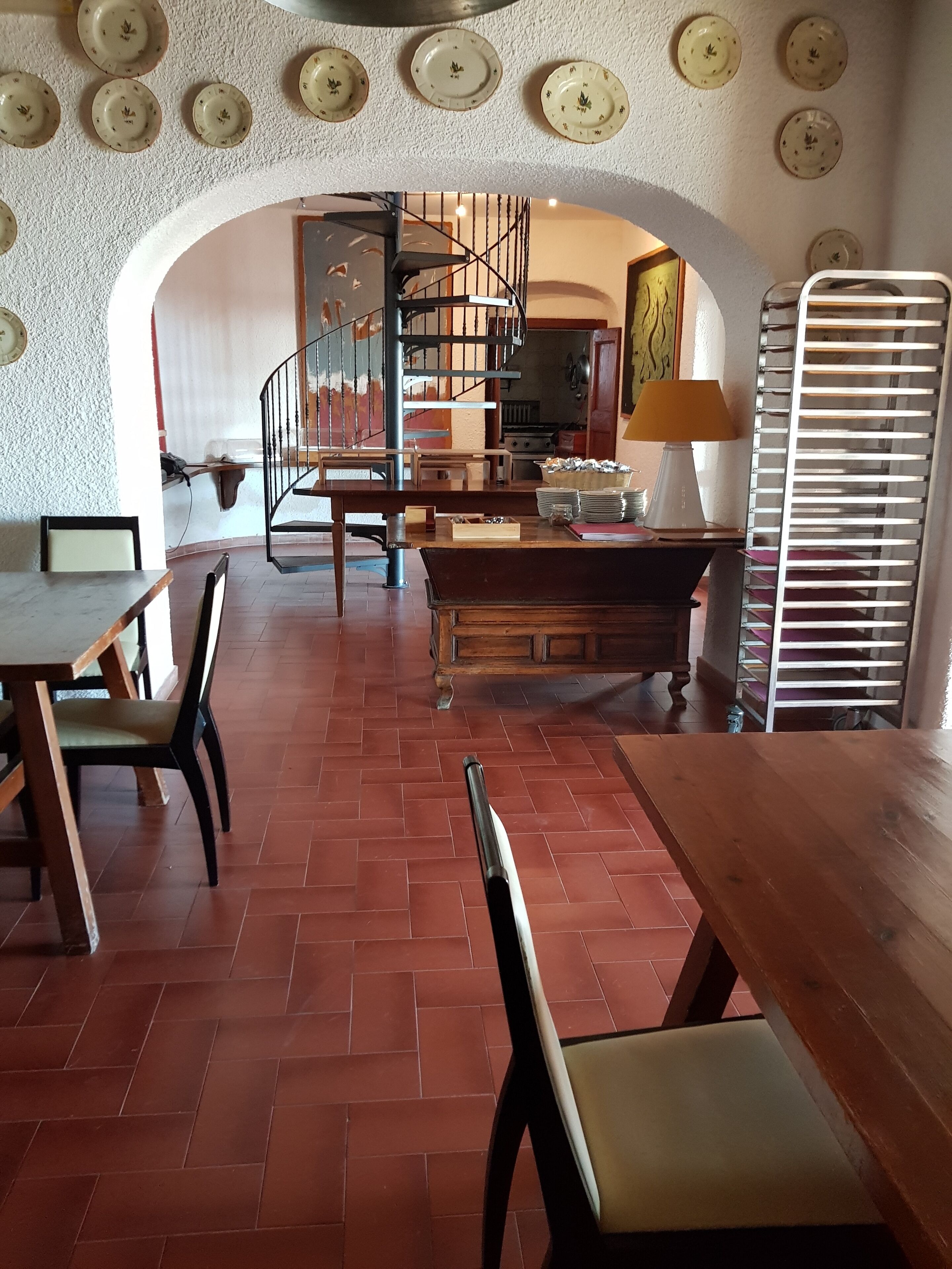 Un'ampia sala da pranzo con un tavolo e sedie in legno, una scala che conduce a un livello superiore e una cucina visibile sullo sfondo.