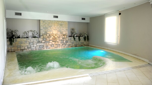 Zona de spa con pared de piedra, un amplio jacuzzi y plantas decorativas.