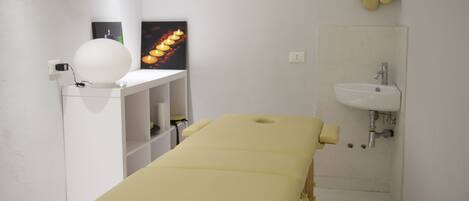 A clinical examination room with a treatment table, a white sink, and a wall-mounted footrest.