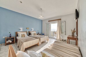 A hotel room with two beds, a desk, a chair, a TV, and a balcony with a view.