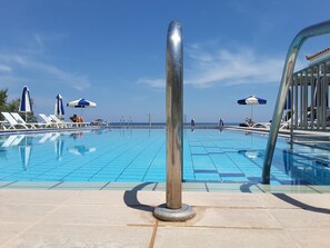 A swimming pool with clear blue tiles, lounge chairs, and umbrellas. - Maria Mare Apart-hotel (Zakynthos)