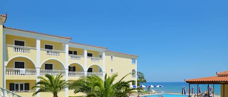 A hotel with a pool, palm trees, and a view of the sea.