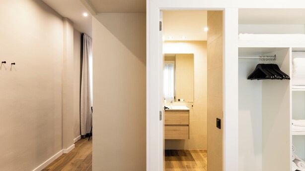 A modern hotel room with a wooden floor, a white wardrobe, and a bathroom with a mirror and sink. - Apartamentos Laforja (Barcelona)
