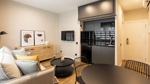 A modern living room with a sofa, a round coffee table, and a dining table with chairs. There is a kitchen area with a refrigerator and a microwave. - Apartamentos Laforja (Barcelona)