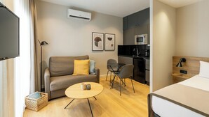 A modern hotel room with a sofa, a small round table, a bed, a kitchenette, and a TV. - Apartamentos Laforja (Barcelona)