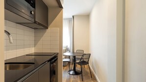 A compact kitchen with a modern stove, a sink, and a dining area with a round table and chairs. - Apartamentos Laforja (Barcelona)
