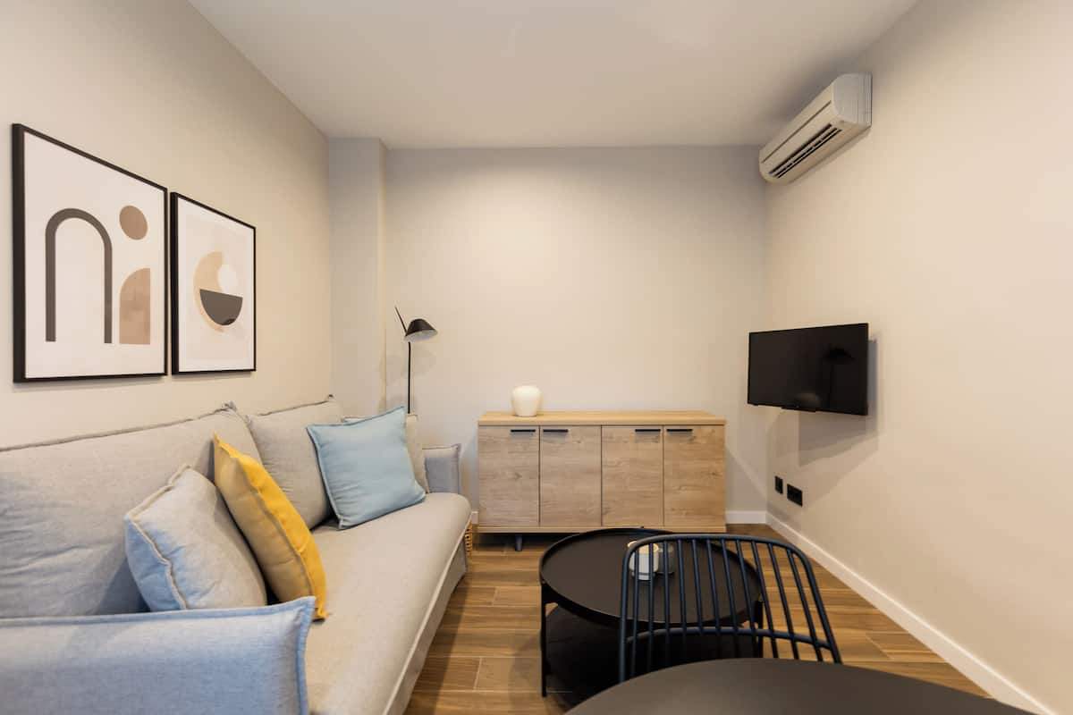A compact living space with a sofa, a dining table, and a TV mounted on the wall.