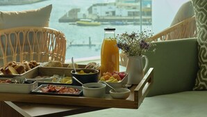 A breakfast tray with food and drinks on a table by a window overlooking a marina. - Octant Ponta Delgada (Ponta Delgada)