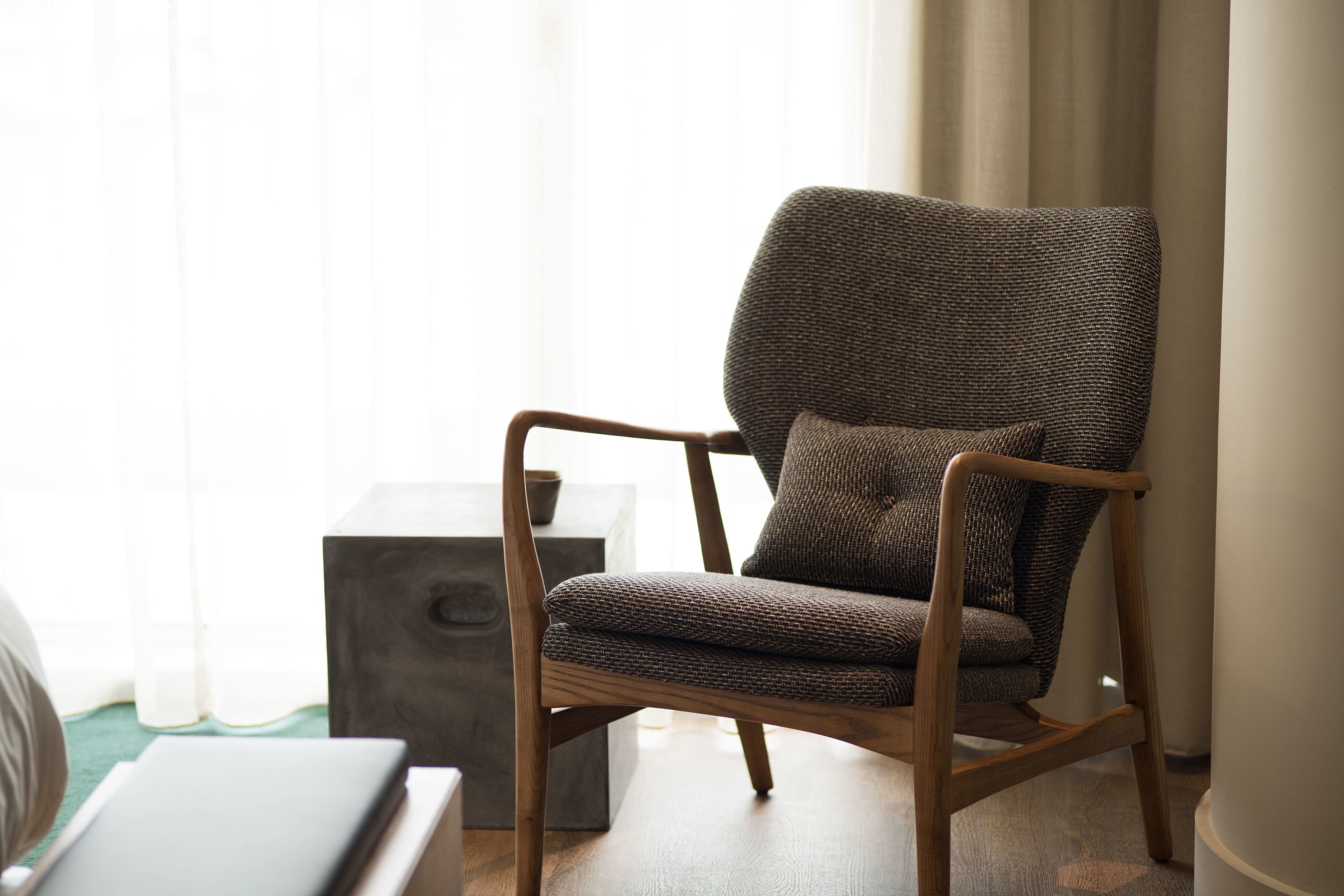 A modern armchair with a woven seat and backrest, positioned next to a wooden side table with a dark cube-shaped object on it.