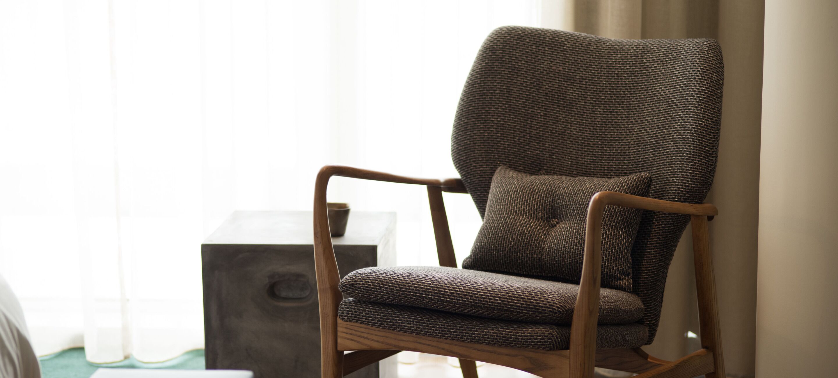 Un sillón de madera con asiento y respaldo tejido, colocado junto a una mesita auxiliar oscura.