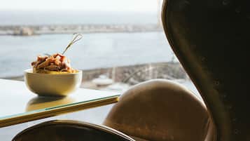 A dining area with a bowl of food on a table, a chair, and a view of the sea.