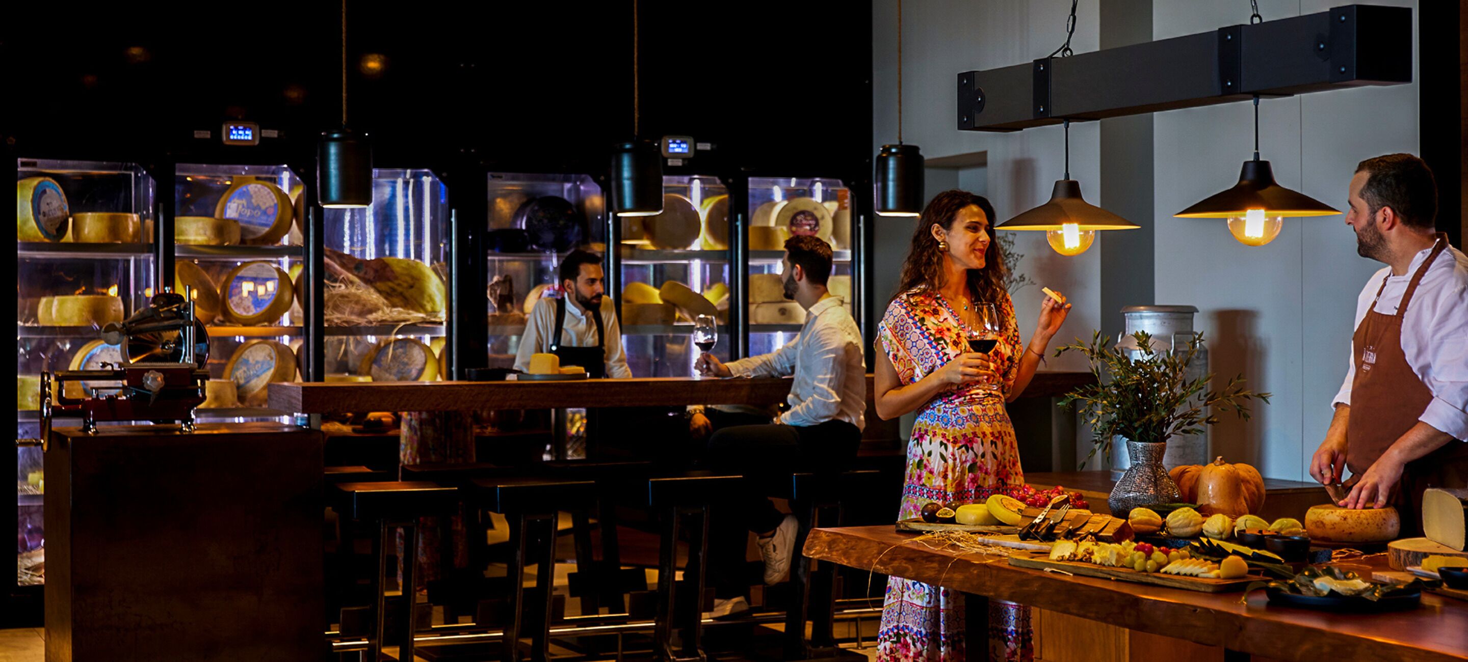 L’intérieur d’un restaurant avec un bar, des meubles en bois et un présentoir de fromages et de fruits.