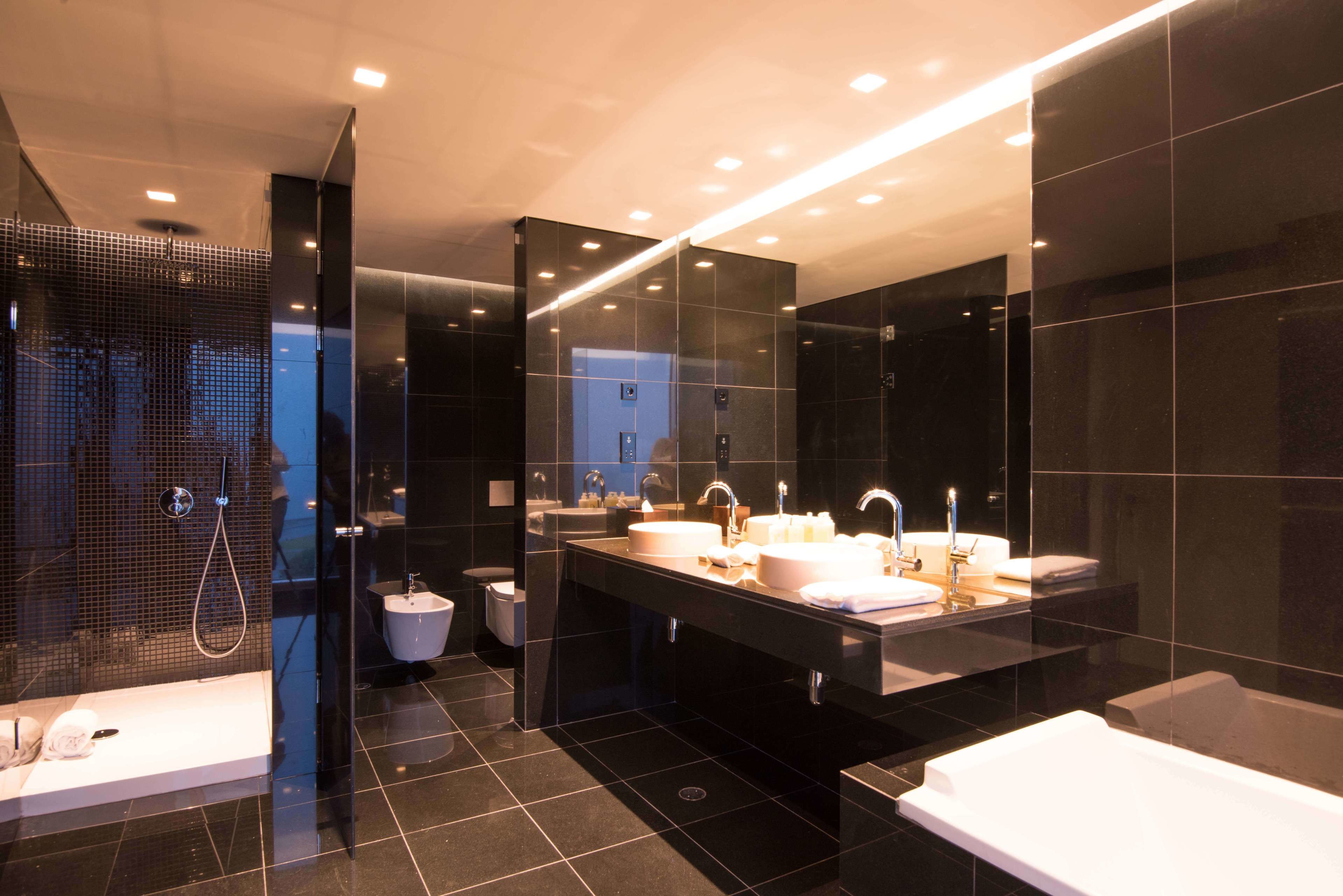 Une salle de bain moderne dotée d’un grand miroir, de deux lavabos, d’une baignoire et d’un espace douche.