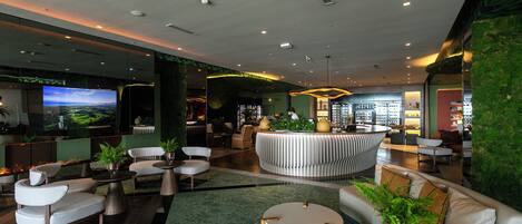 A modern lobby with a large TV, seating areas, and a bar.