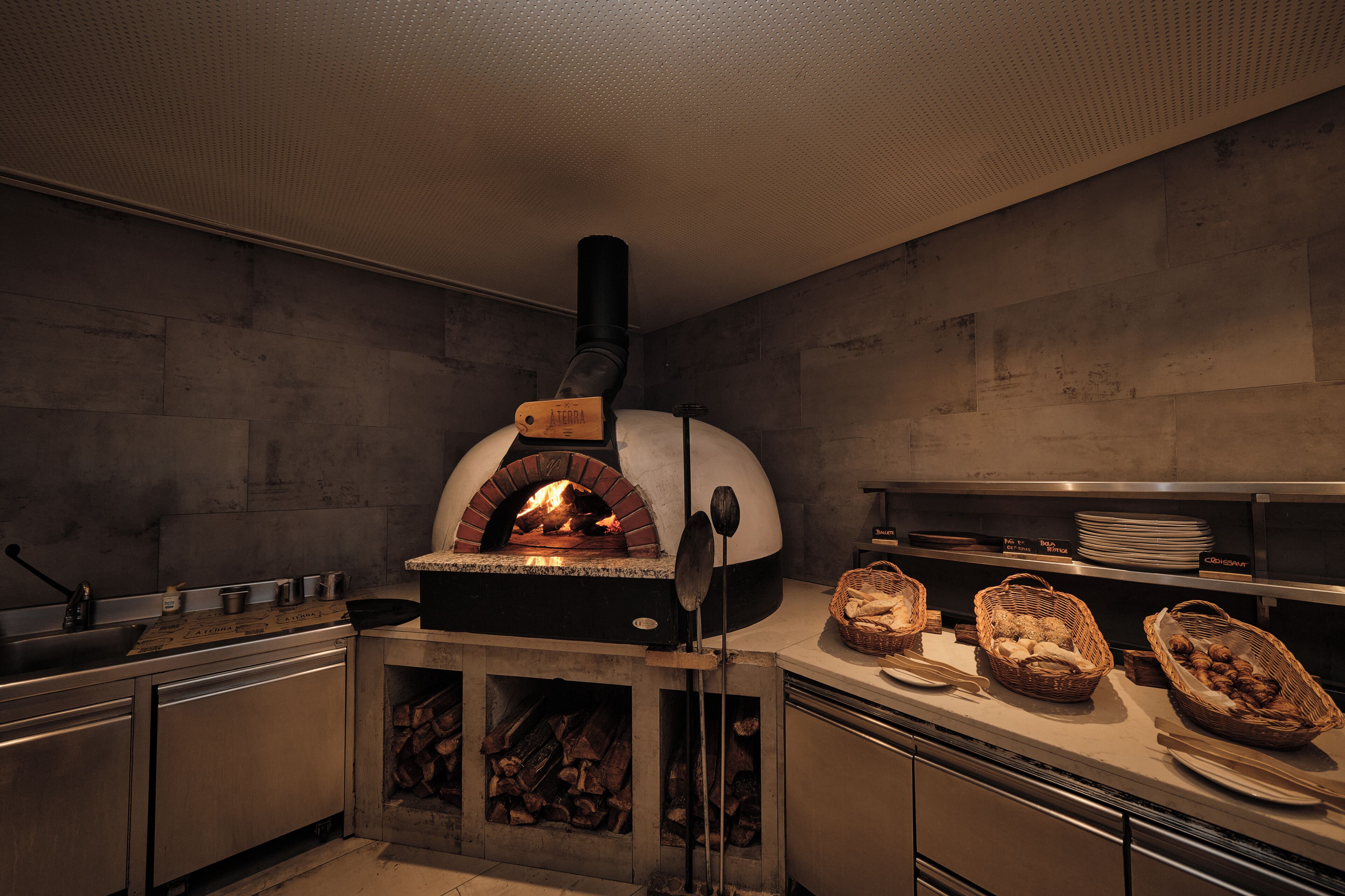 A kitchen with a wood-fired oven, a sink, and baskets of bread on the counter.