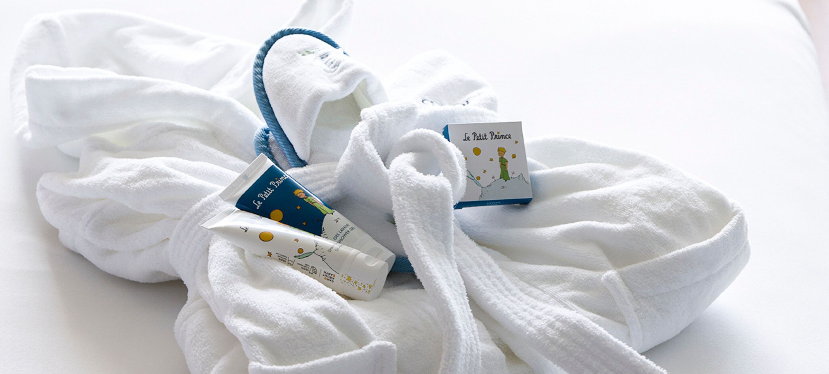 A white bathrobe with a blue trim and two small books titled 'Le Petit Prince' and 'Le Petit Prince' on a white surface.