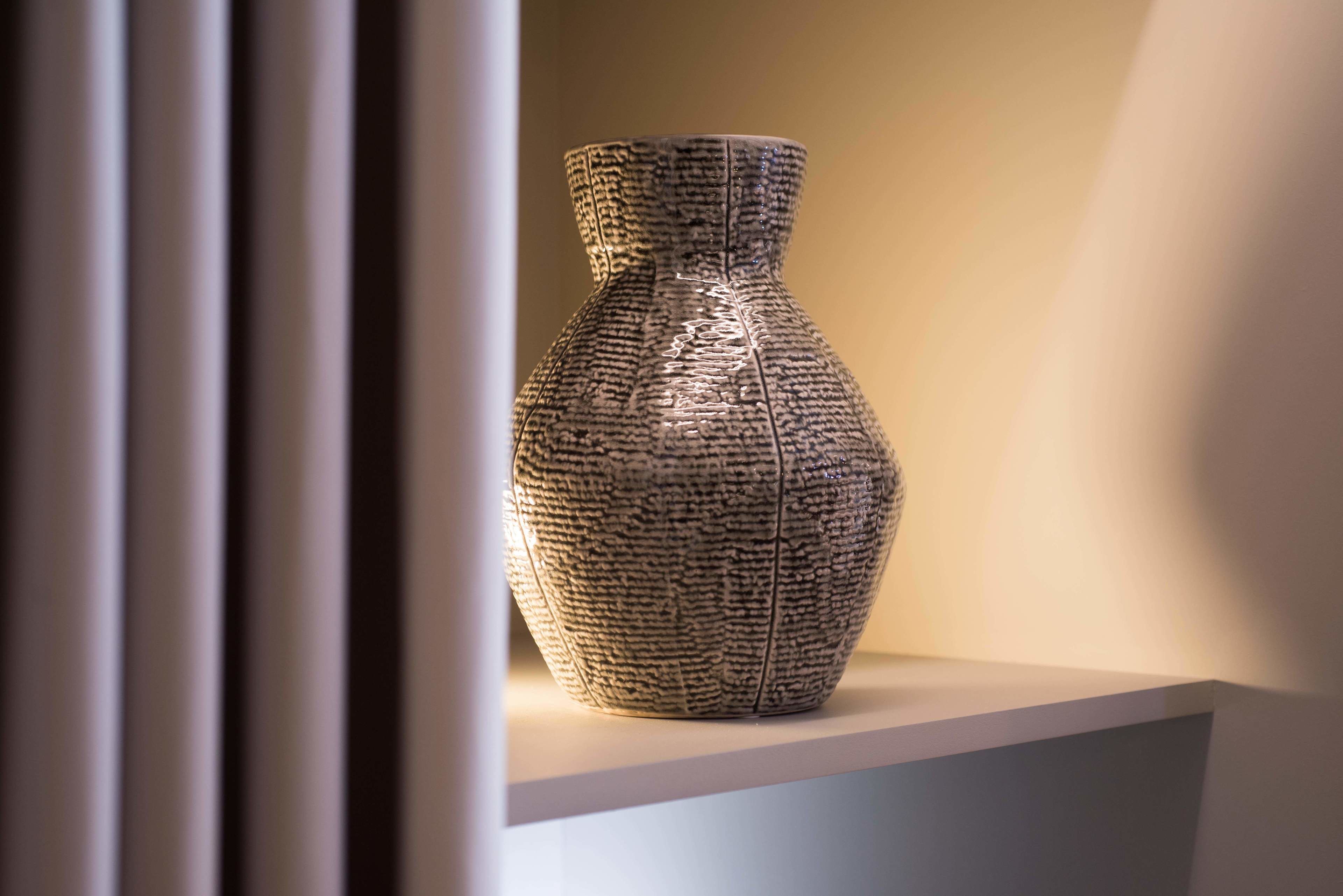 A textured vase on a white pedestal in a well-lit display area.