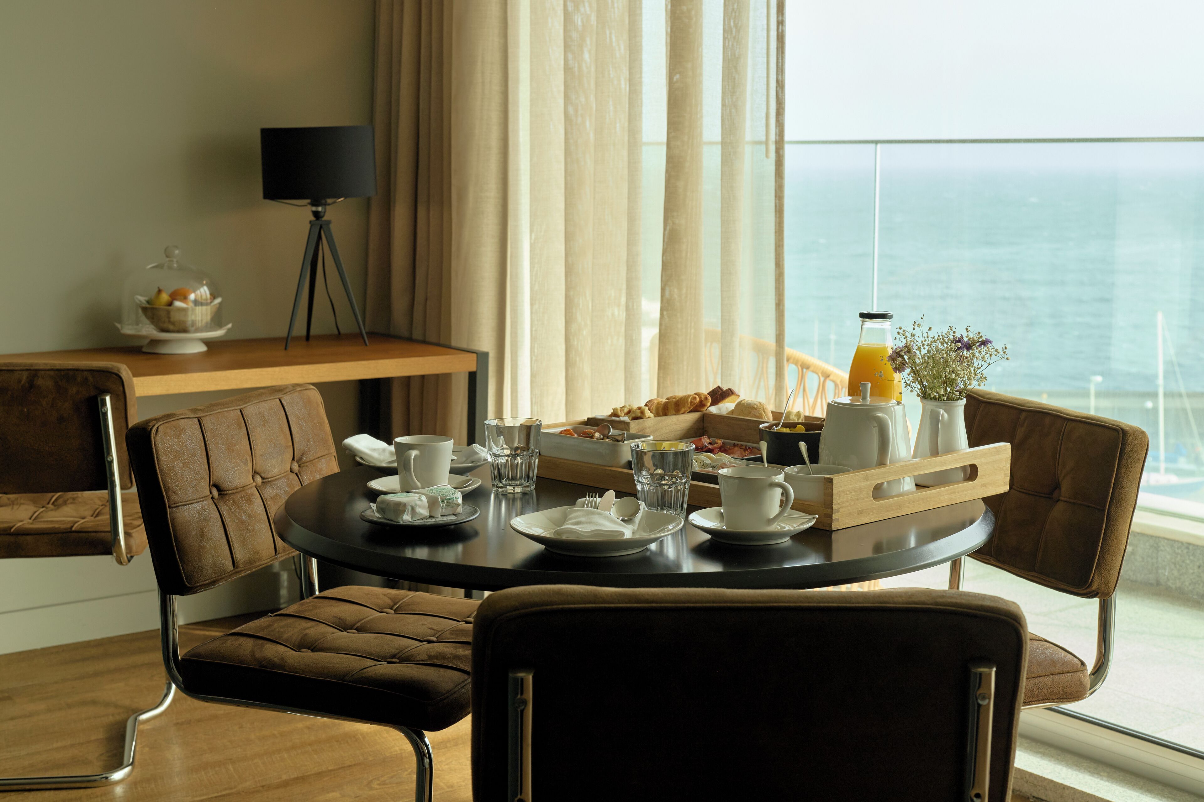 A dining area with a table set for breakfast, including plates, cups, and a fruit basket.