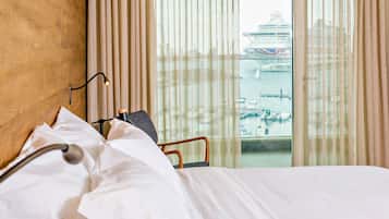 Habitación de hotel con cama, lámpara de noche y vista a un crucero y puerto deportivo.