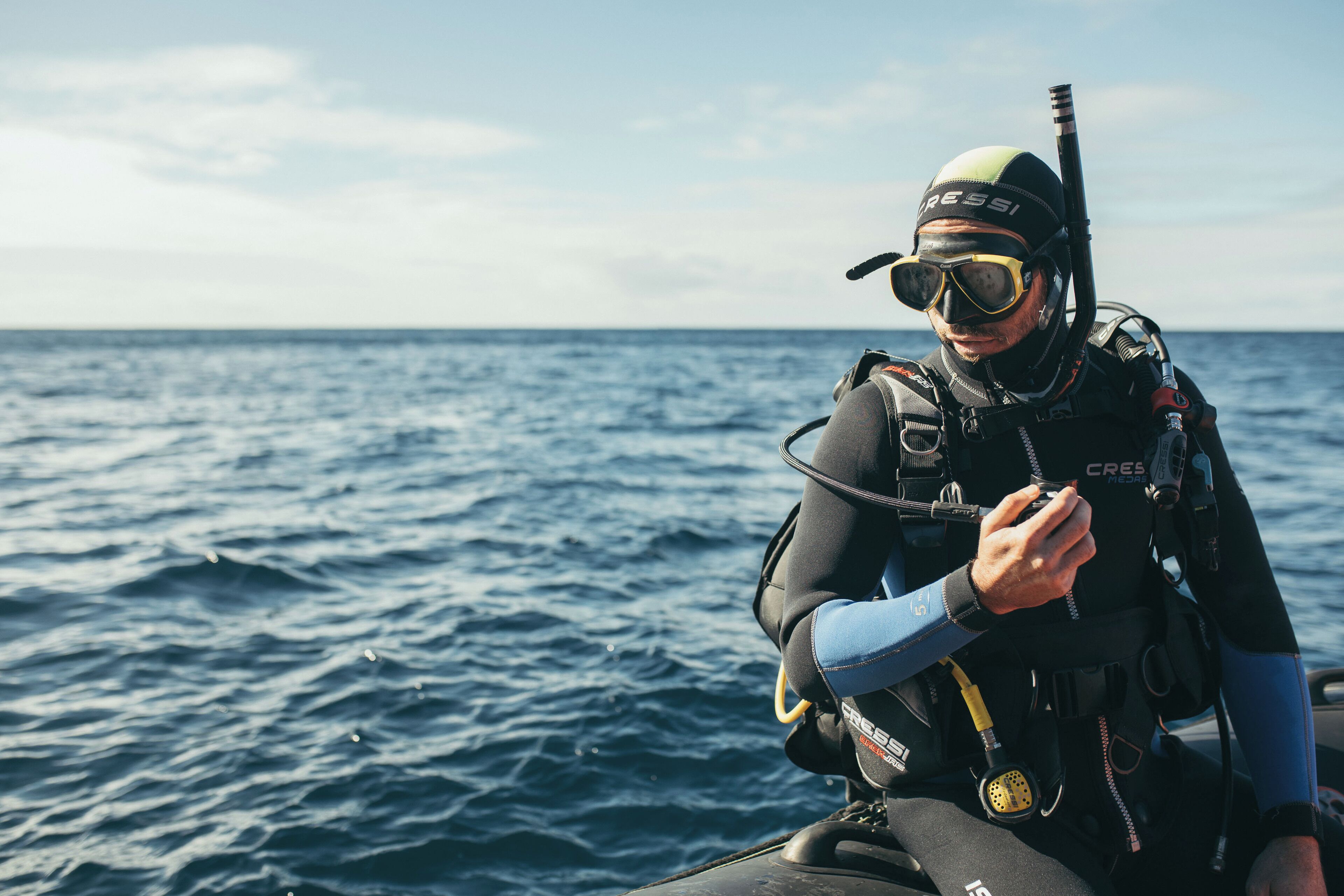 A person in scuba diving gear on a boat, with the ocean in the background.