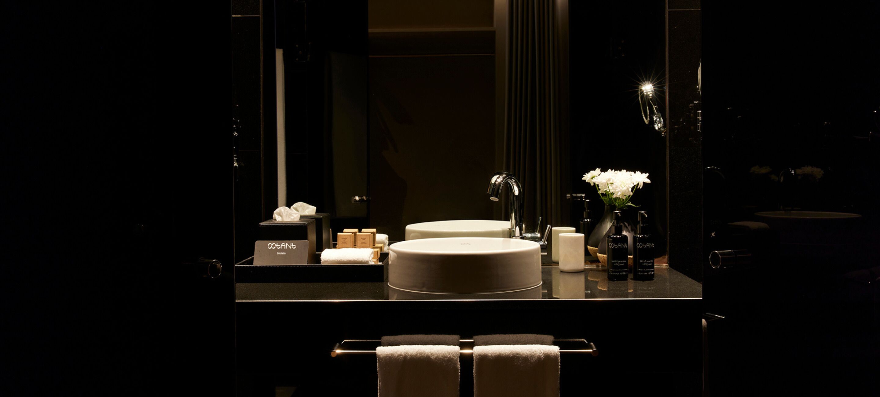 A modern bathroom with a round sink, a mirror, and a vase with white flowers.