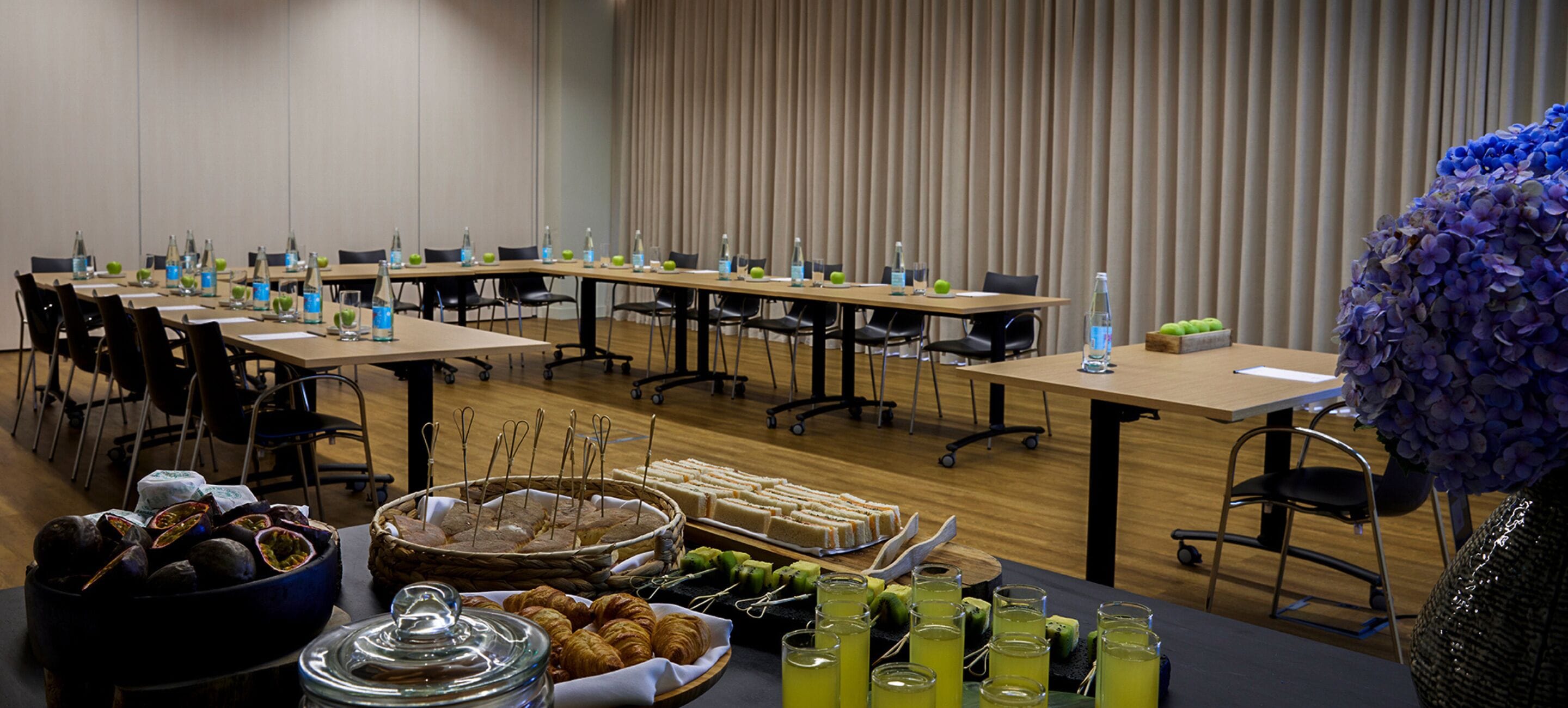 A conference room with long tables, chairs, and a buffet with food and drinks.