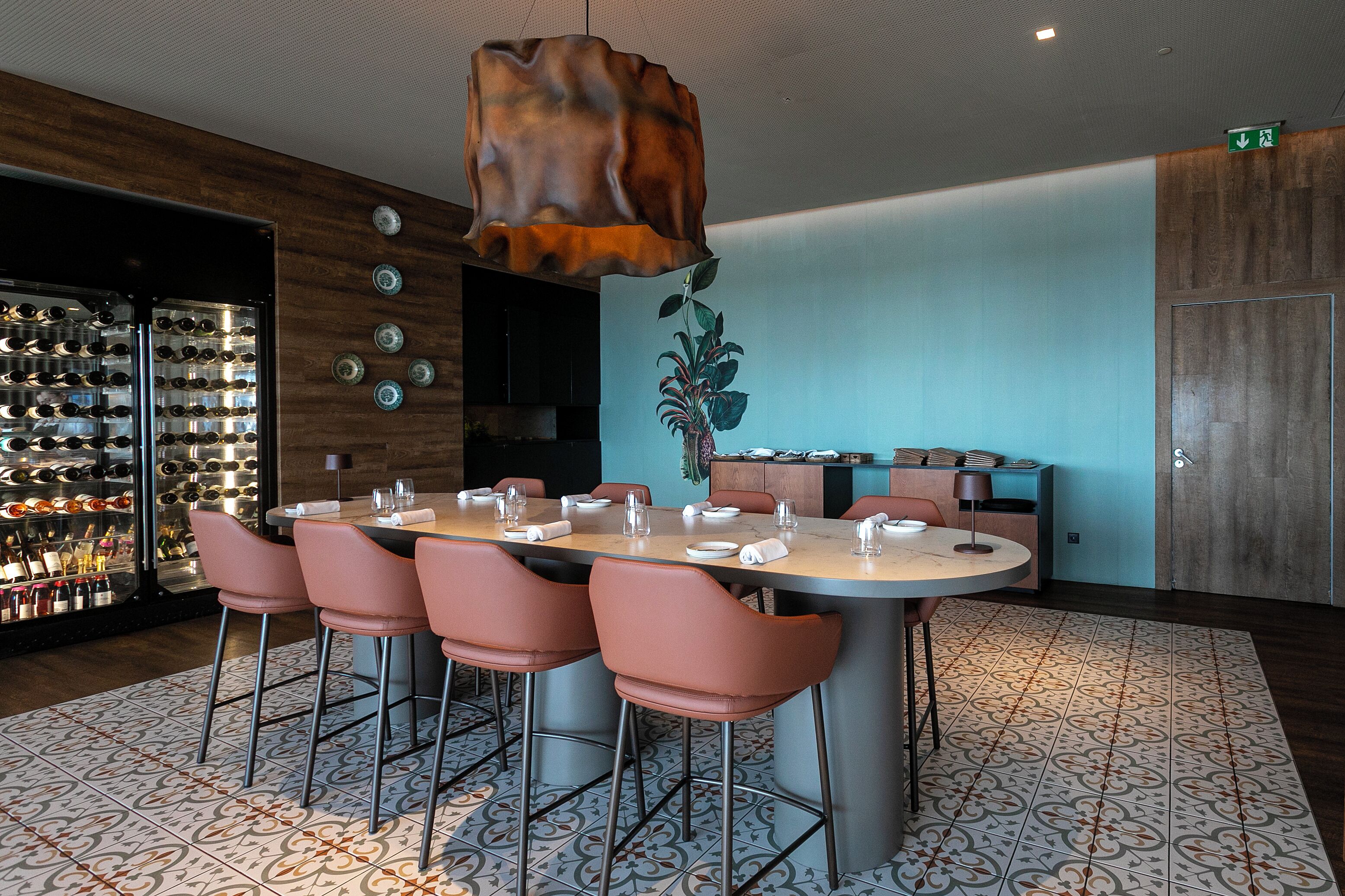 A dining area with a round table, pink chairs, and a wine rack in the background.