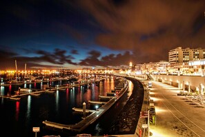 A marina at night with boats docked, a curved walkway, and buildings in the background. - Octant Ponta Delgada (Ponta Delgada)