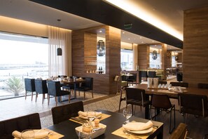 A modern dining area with tables set for four, large windows offering a view of the city, and a bar area with a counter and seating. - Octant Ponta Delgada (Ponta Delgada)