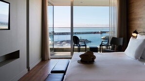 A hotel room with a large bed, a view of the sea and a pier, a small table with chairs, and a lamp. - Octant Ponta Delgada (Ponta Delgada)
