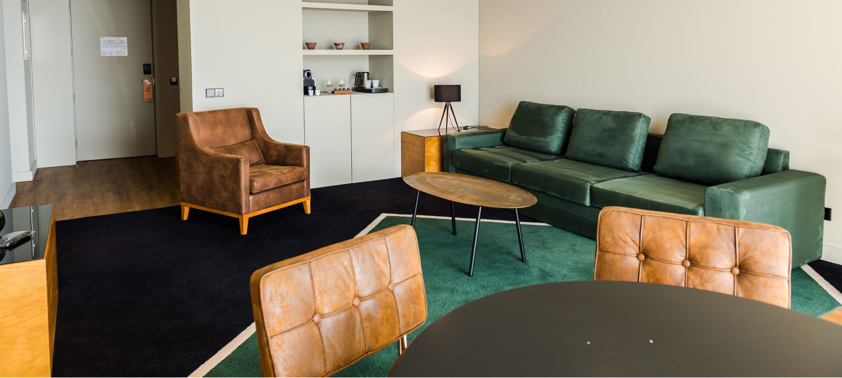 A modern living room with a brown leather armchair, a green sofa, and a round coffee table.