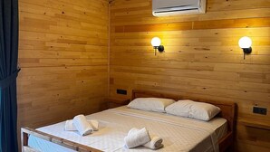 A wooden room with a bed, two wall-mounted lights, and an air conditioning unit. - Cirali Simge Holiday Houses (Kemer)