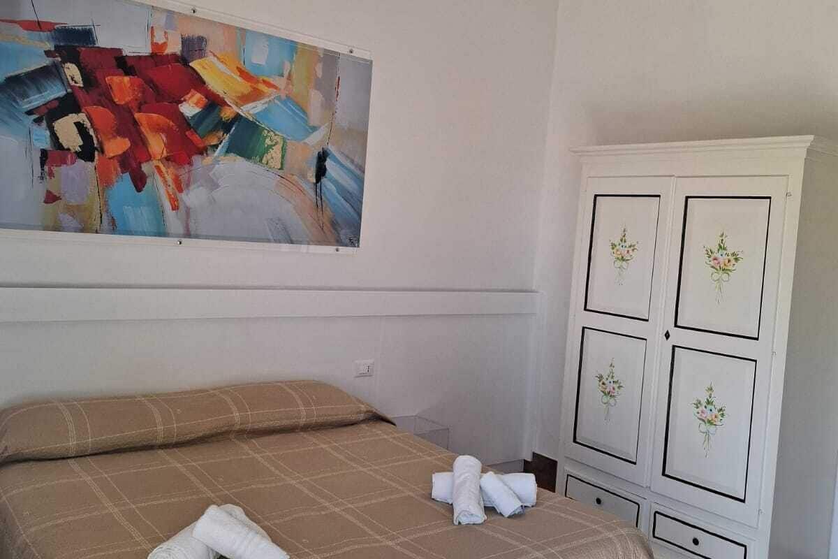 Habitación de hotel con un cuadro abstracto grande, una cama con colcha color beige y un armario blanco con diseños florales.